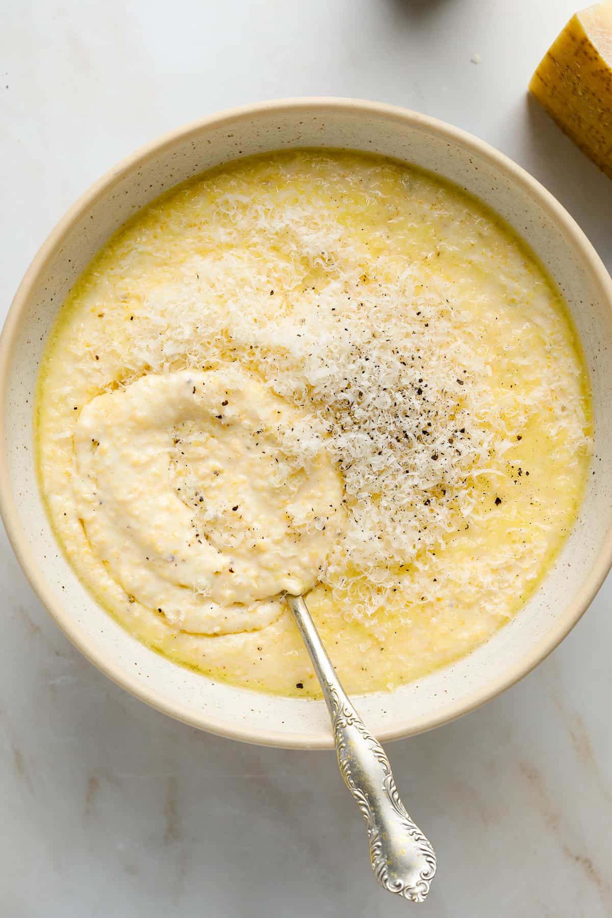 A white speckled ceramic bowl filled with cooked polenta and topped with grated parmesan cheese.