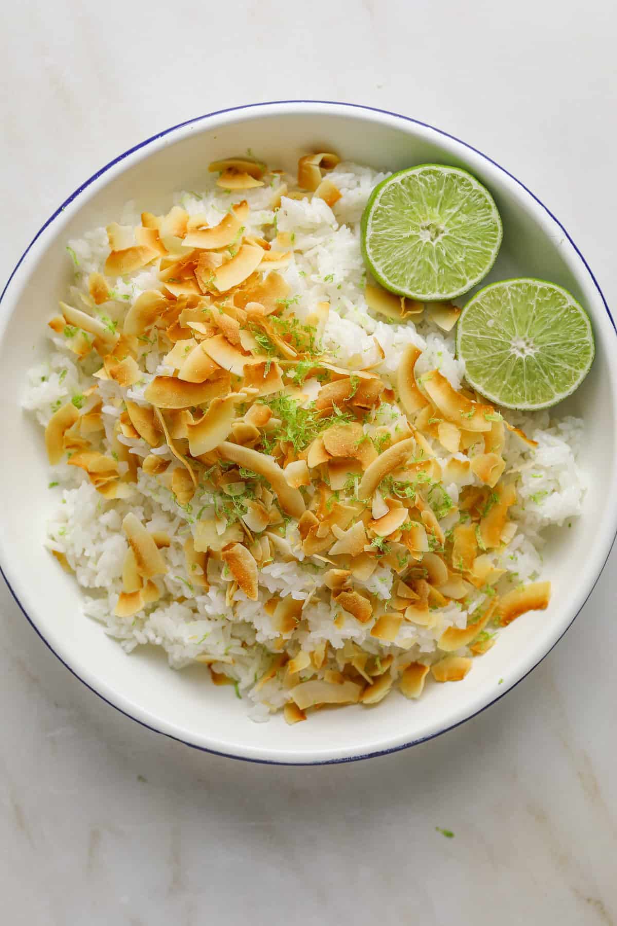 A bowl of rice, coconut and two halves of lime on a marble tabletop.