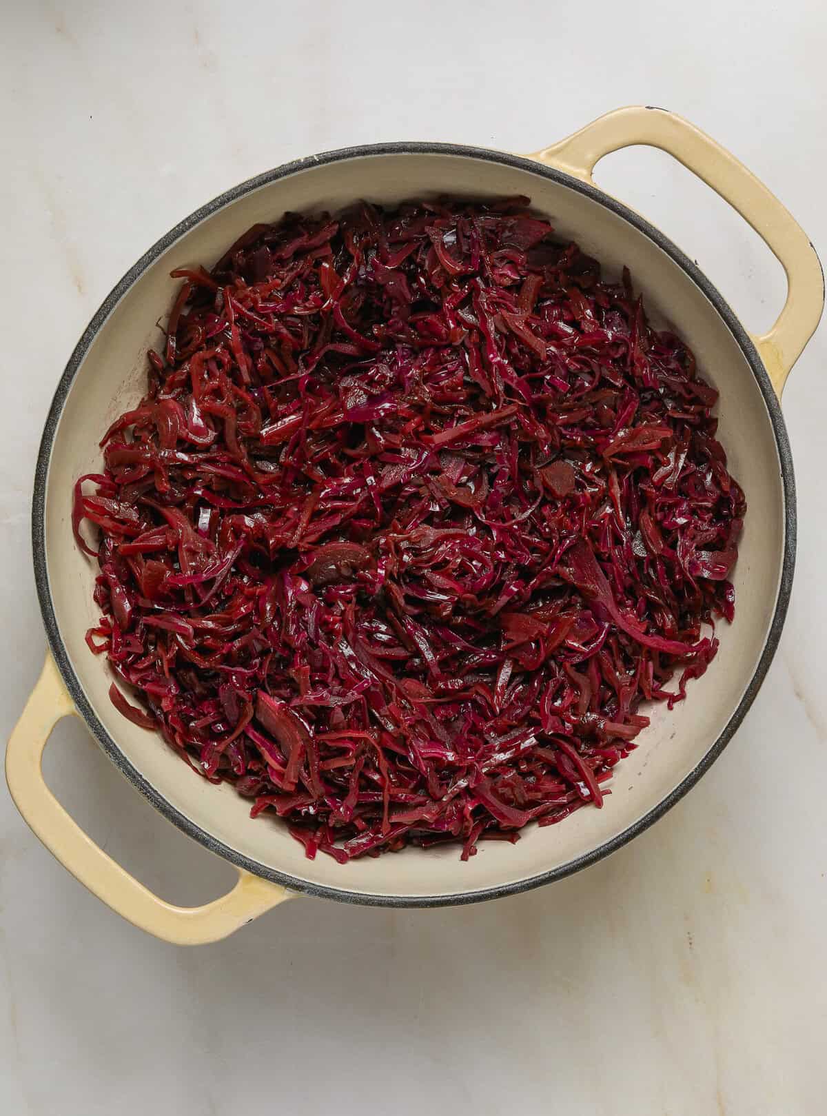 Cooked red cabbage in a beige dutch oven.