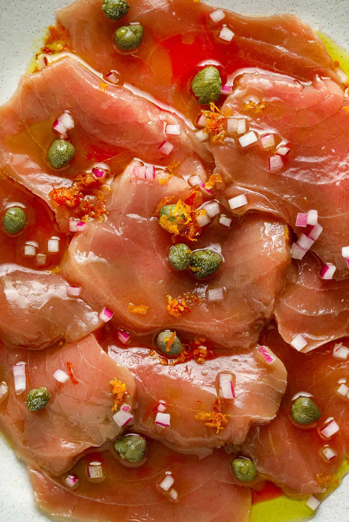 Close up image of sliced, raw fish, capers and minced onion.