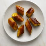 Pieces of golden, fried plantains on a small white plate on a marble tabletop.