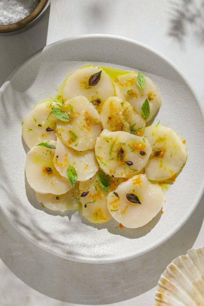 Slices of raw scallop on a white plate.
