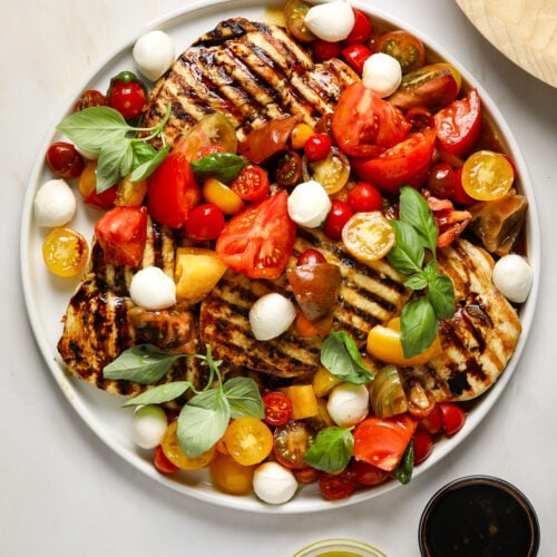 A large white platter filled with grilled chicken, red and yellow tomatoes, fresh basil and mozzarella cheese.