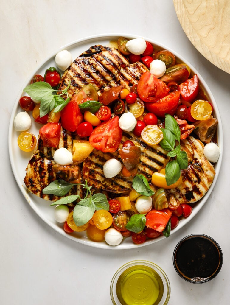 A large white platter filled with grilled chicken, red and yellow tomatoes, fresh basil and mozzarella cheese.