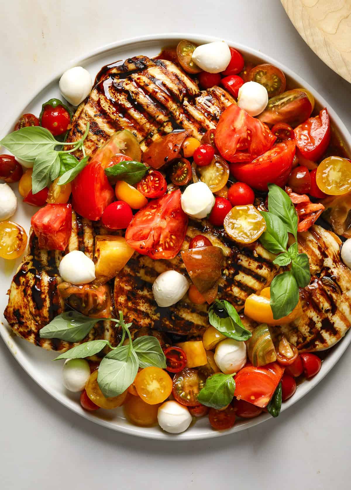 Grilled chicken breast glistening with balsamic glaze, chopped tomatoes and garlic on a white platter.