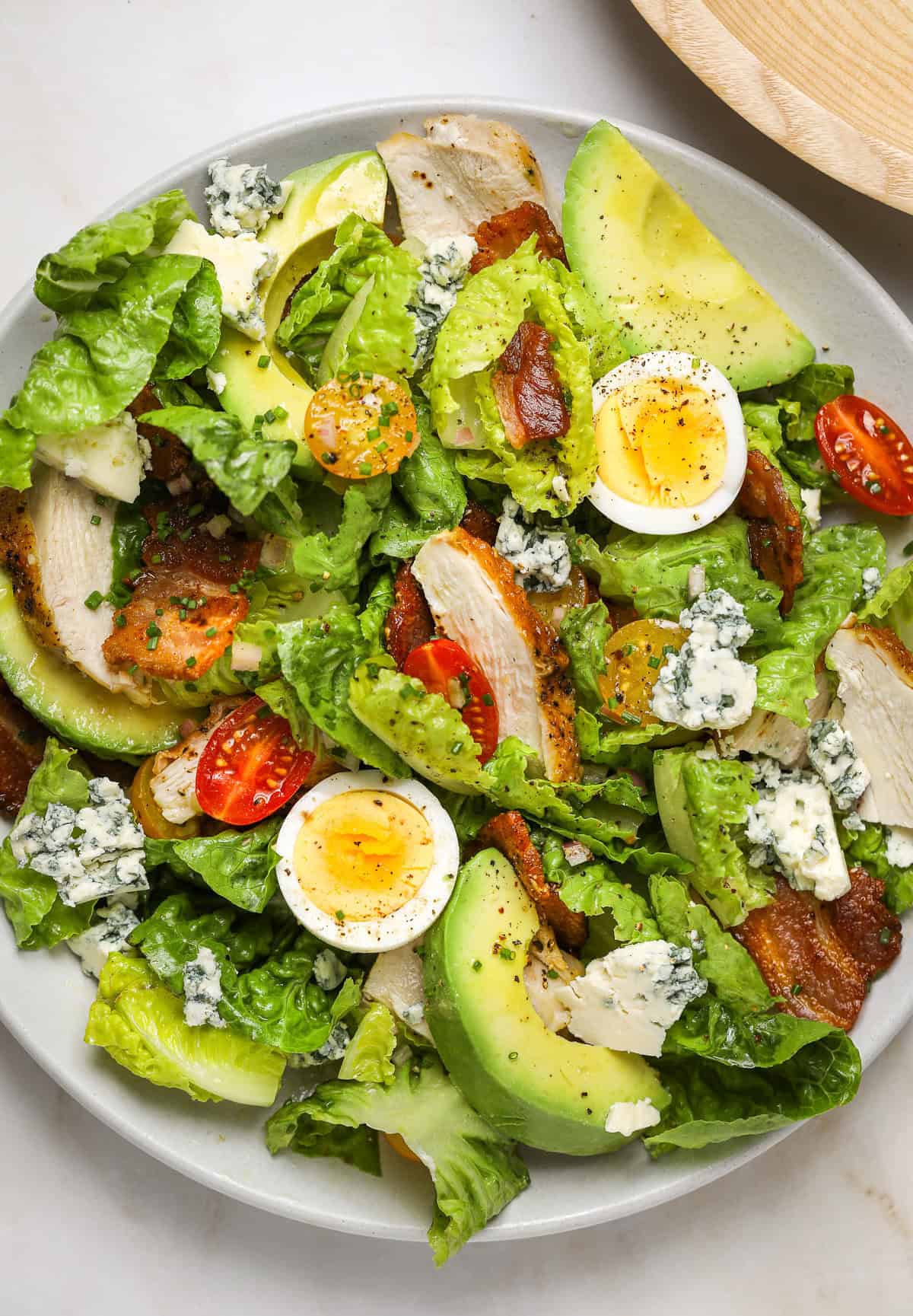 A close up image of a Cobb salad filled with grilled chicken, bacon pieces, avocado slices and crumbled blue cheese.