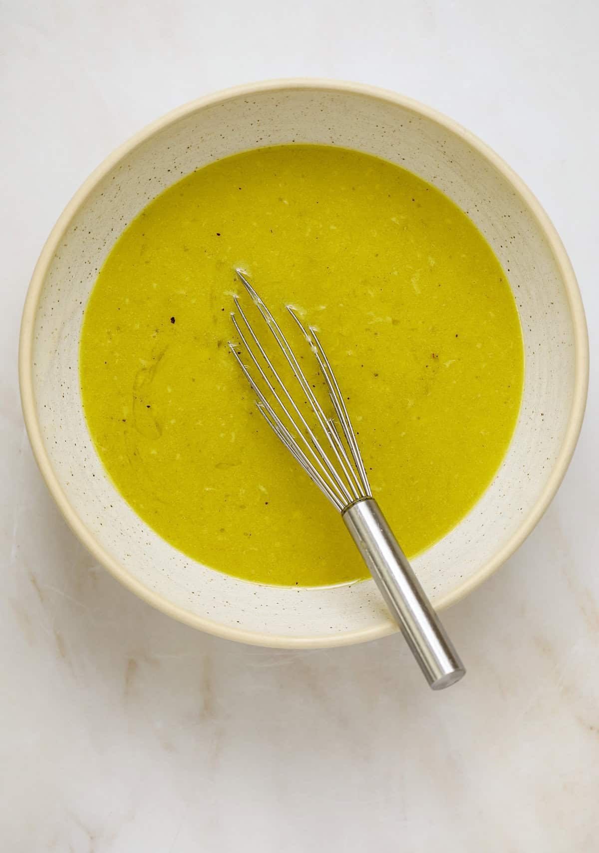 A bright yellow vinaigrette in a ceramic bowl with a metal whisk.