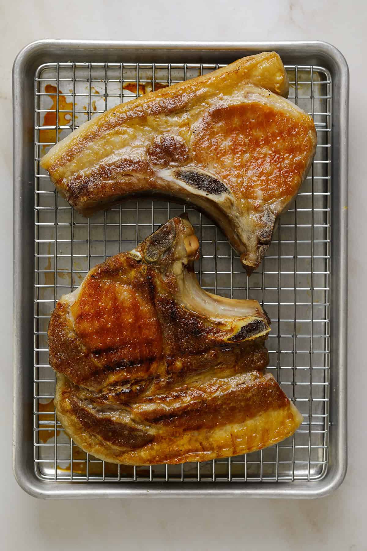 Two grilled, bone-in pork chips on a baking rack.