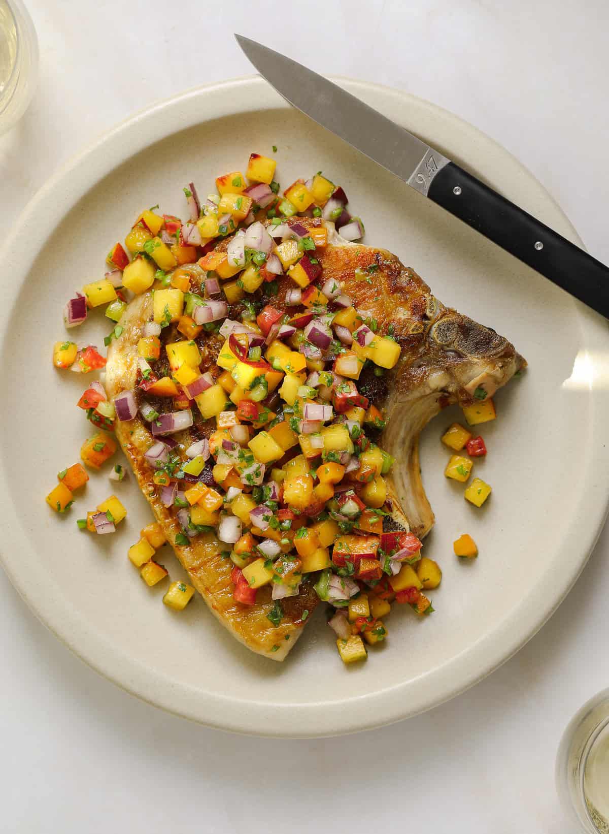 A large pork chip topped with peach salsa on a beige plate.