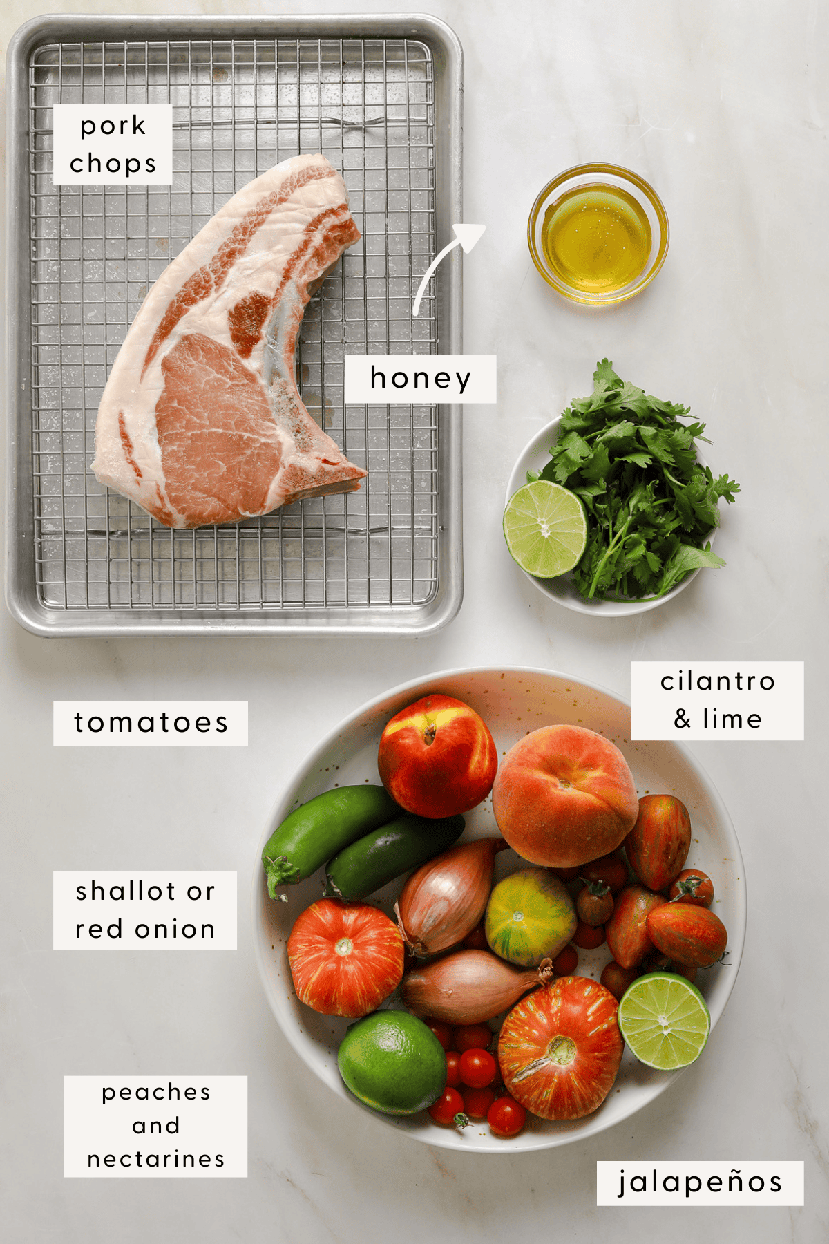 A raw, bone-in pork chip on a baking tray, heirloom tomatoes, peaches, limes and shallots in a bowl.