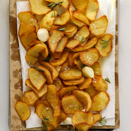 a paper towel lined baking tray filled with fried potatoes, garlic cloves and rosemary.