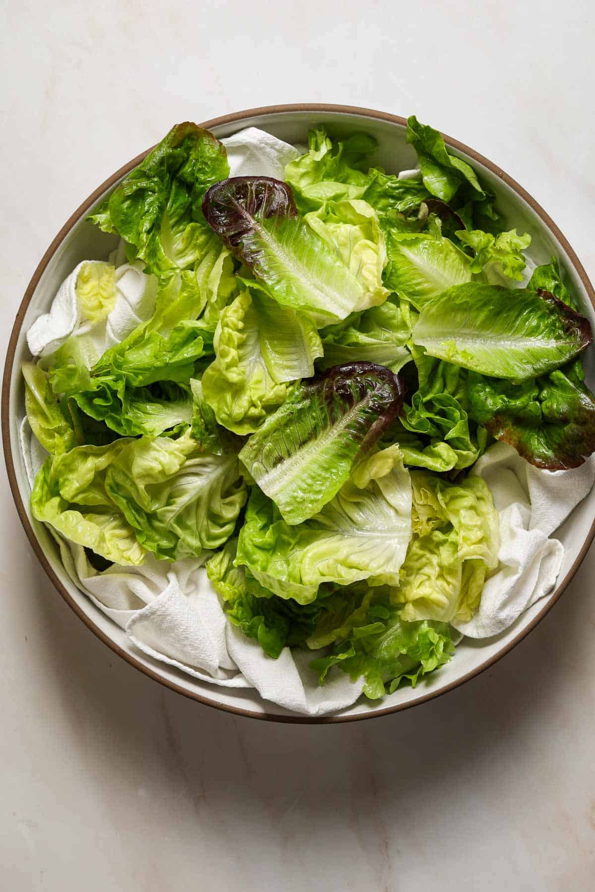 Lettuce leaves drying on a white dish towel in a large bowl.