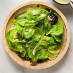 A salad in a wooden bowl on a marble tabletop.