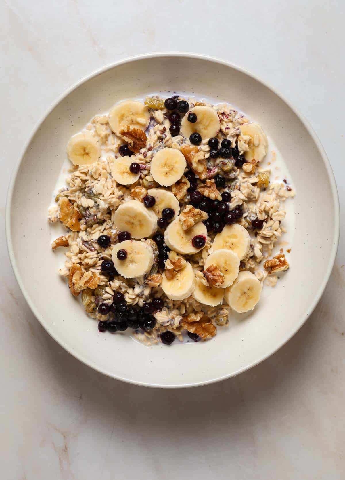 A bowl of oats, sliced banana, blue berries and walnuts.