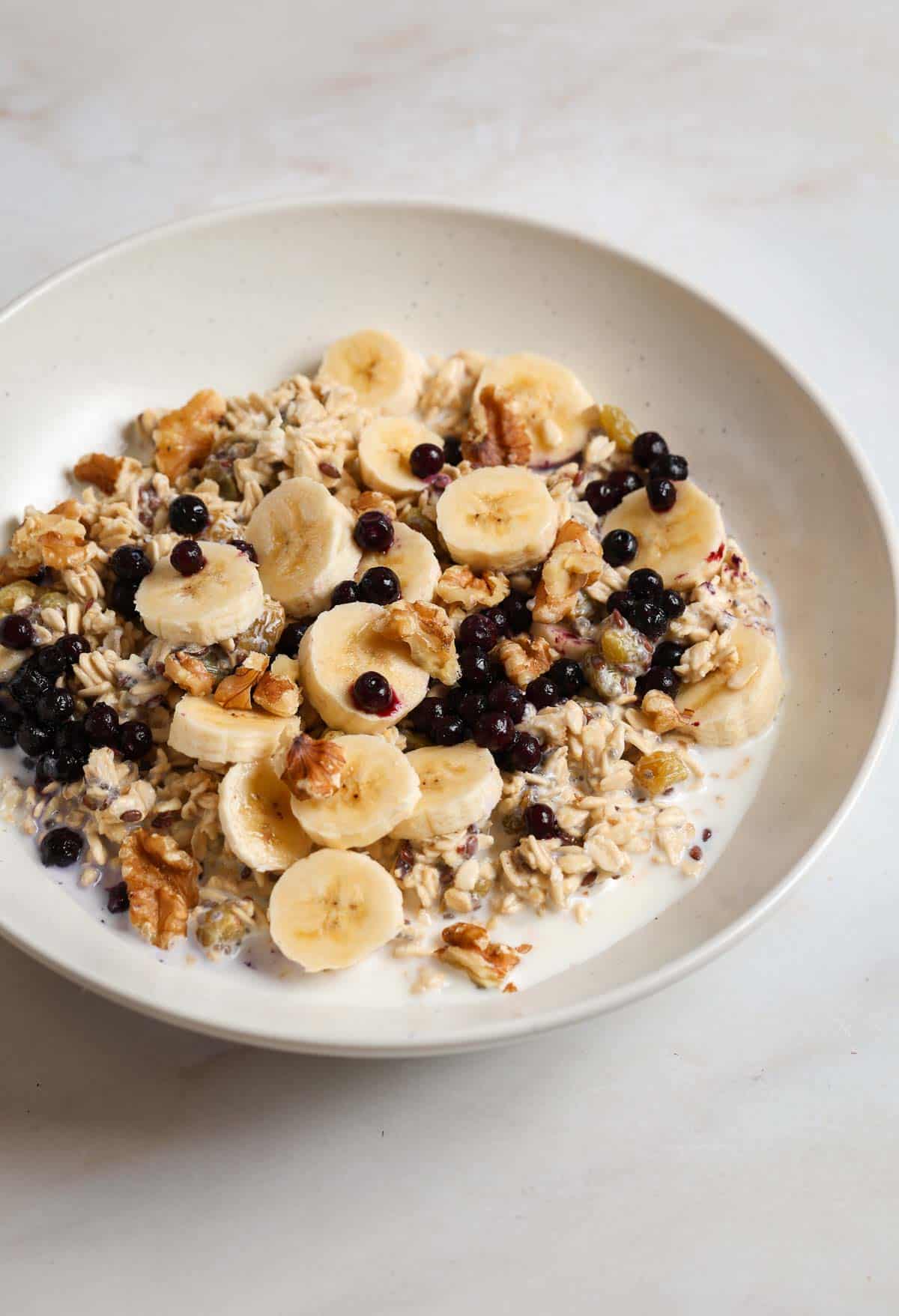 A close up bowl of overnight oats topped with banana slices, walnuts and blueberries.