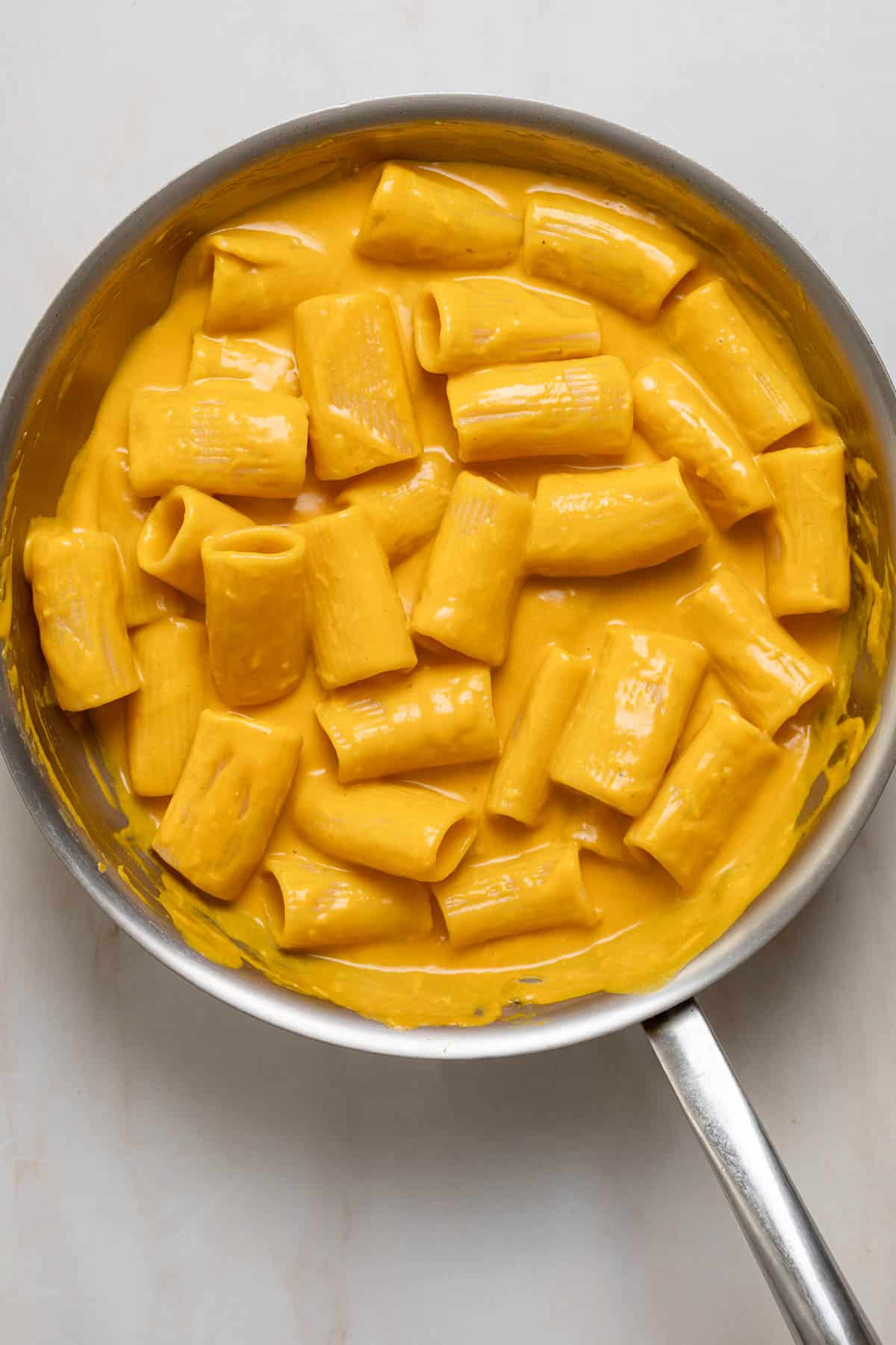 A sauté pan filled with pasta in a creamy orange sauce.