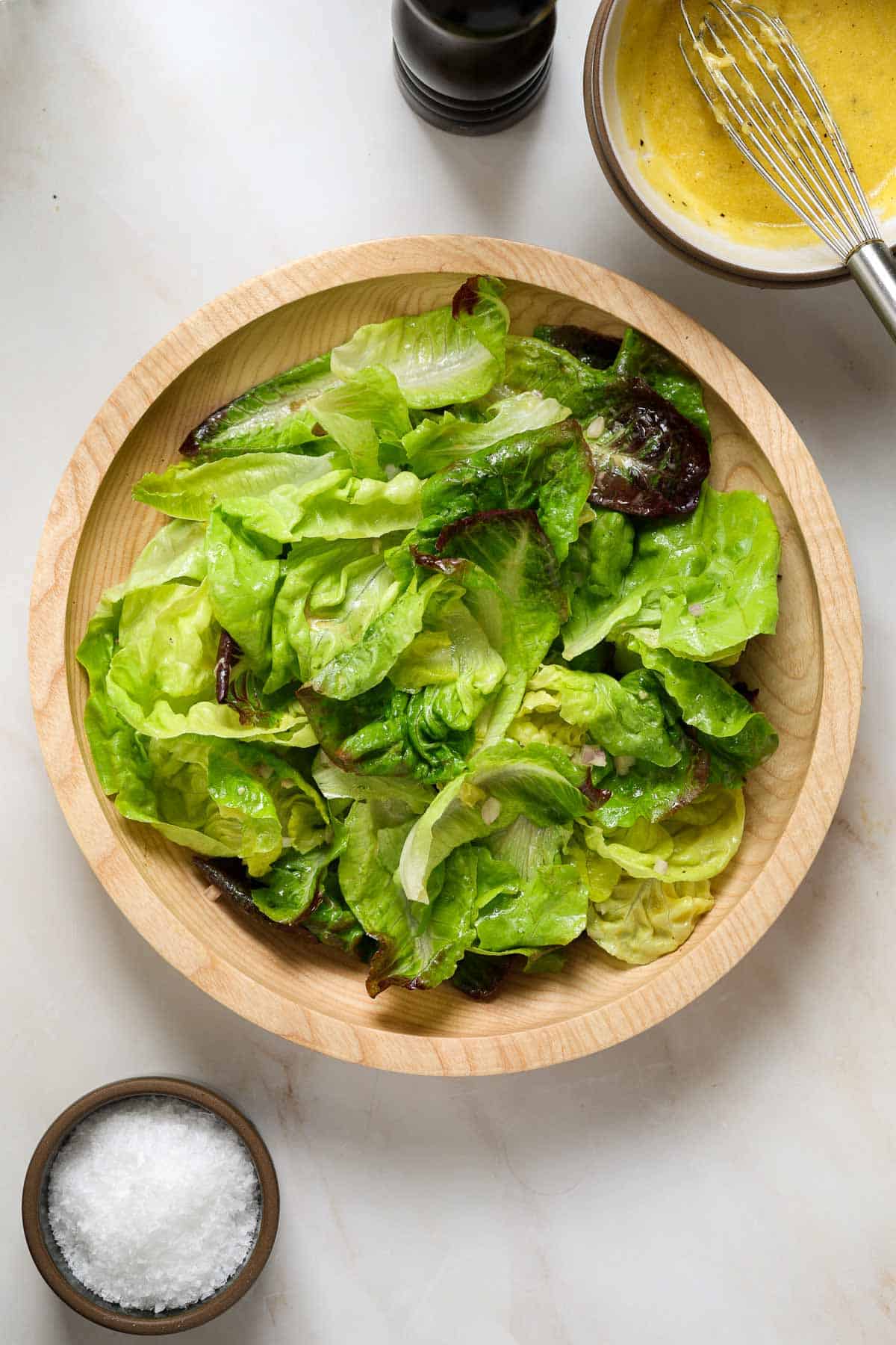 A wooden salad bowl filled with lettuce, salt in a dish on the side.