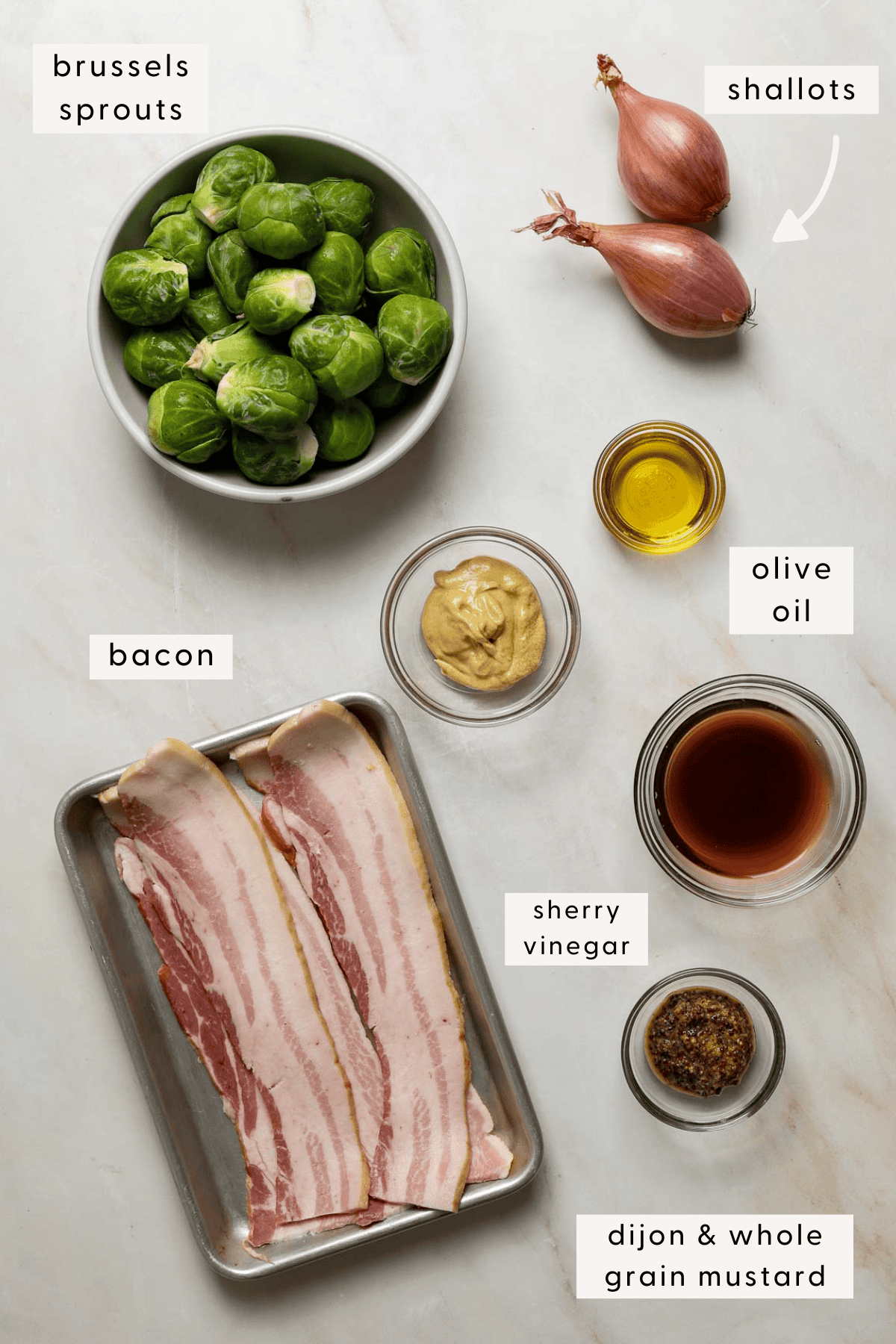 Raw brussels sprouts in a bowl, raw bacon slices on a sheet tray, small dishes of olive oil, mustard and vinegar.