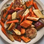 A round platter filled with roasted sweet potatoes, carrots, parsnips, shallots and herbs.