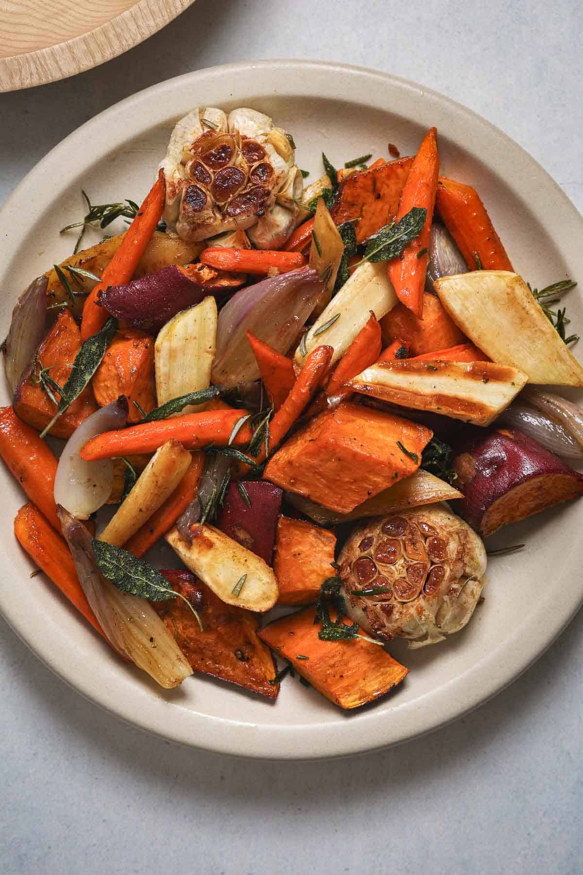 A round platter filled with roasted sweet potatoes, carrots, parsnips, shallots and herbs.