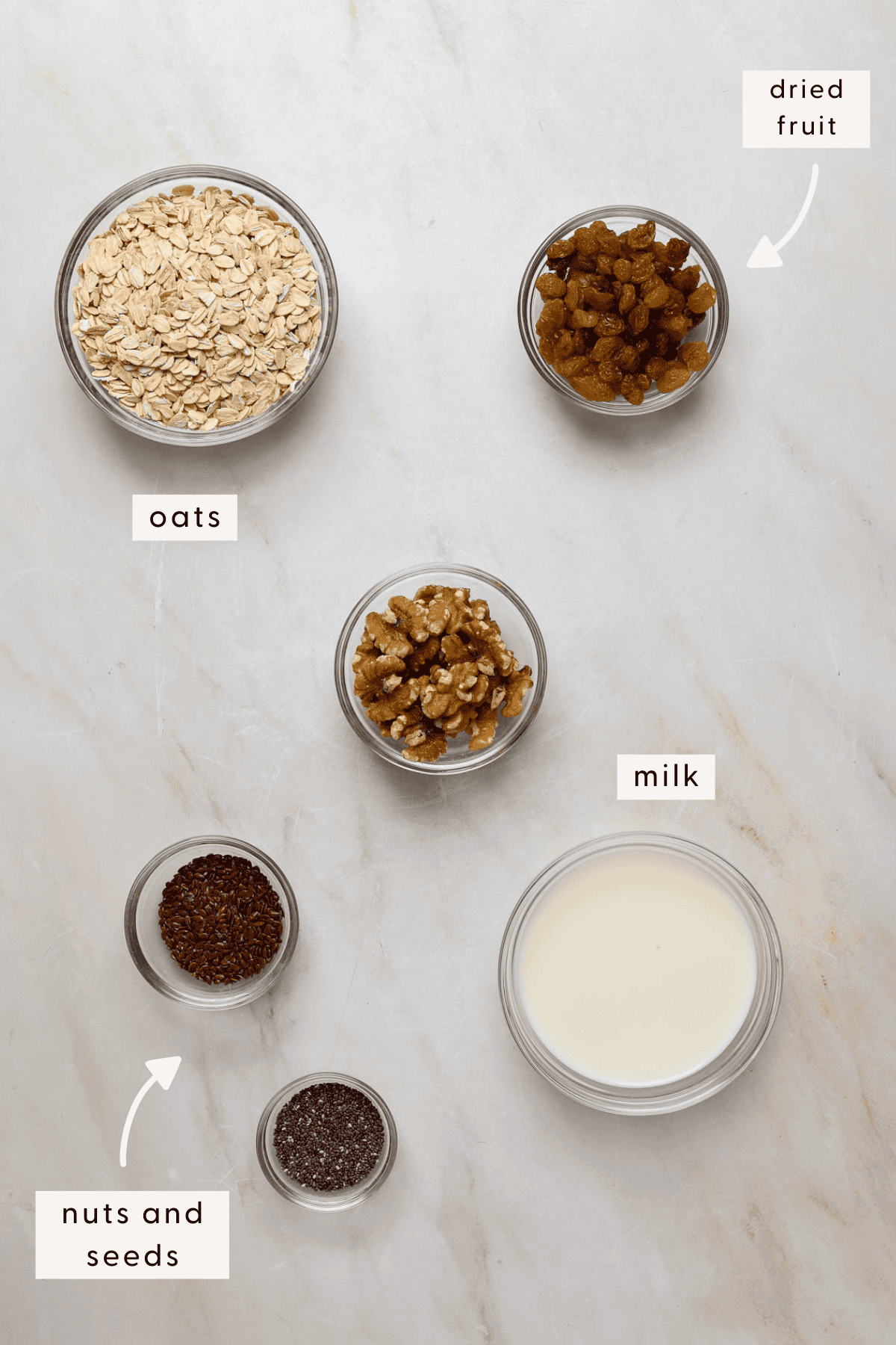 A small bowl of rolled oats, tiny bowls of walnuts, flax seeds, chia and milk.