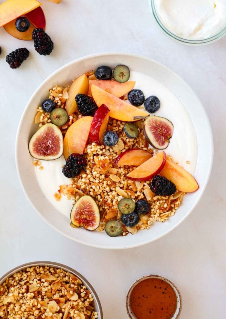 A bowl of granola and yogurt surrounded by a small dish of honey and a jar of yogurt.