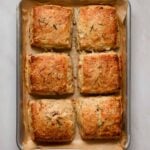 Six, freshly baked (square) savory scones on a brown parchment lined baking tray.