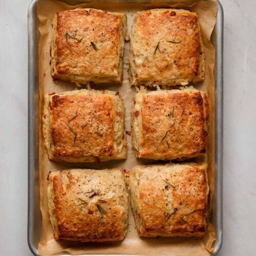 Six, freshly baked (square) savory scones on a brown parchment lined baking tray.