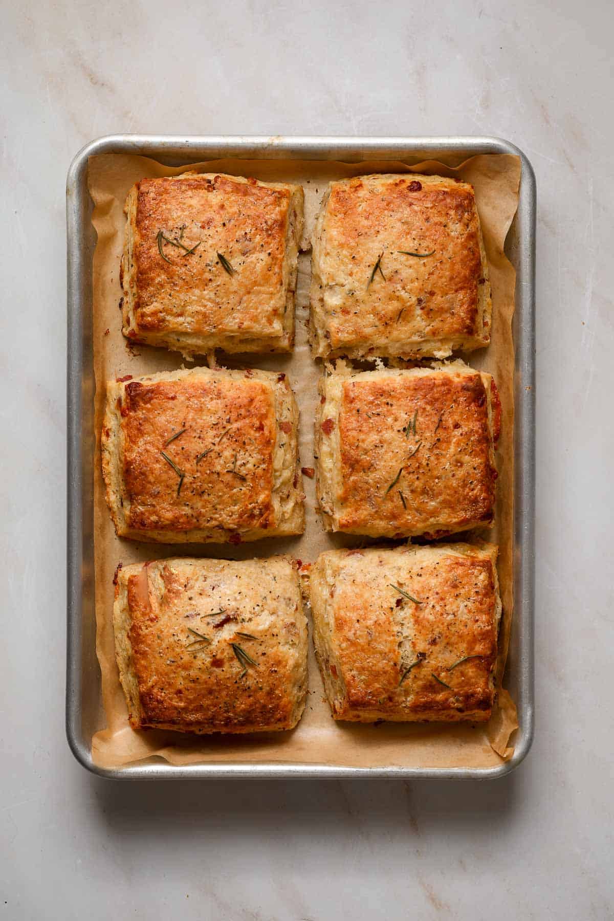 Six, freshly baked (square) savory scones on a brown parchment lined baking tray.