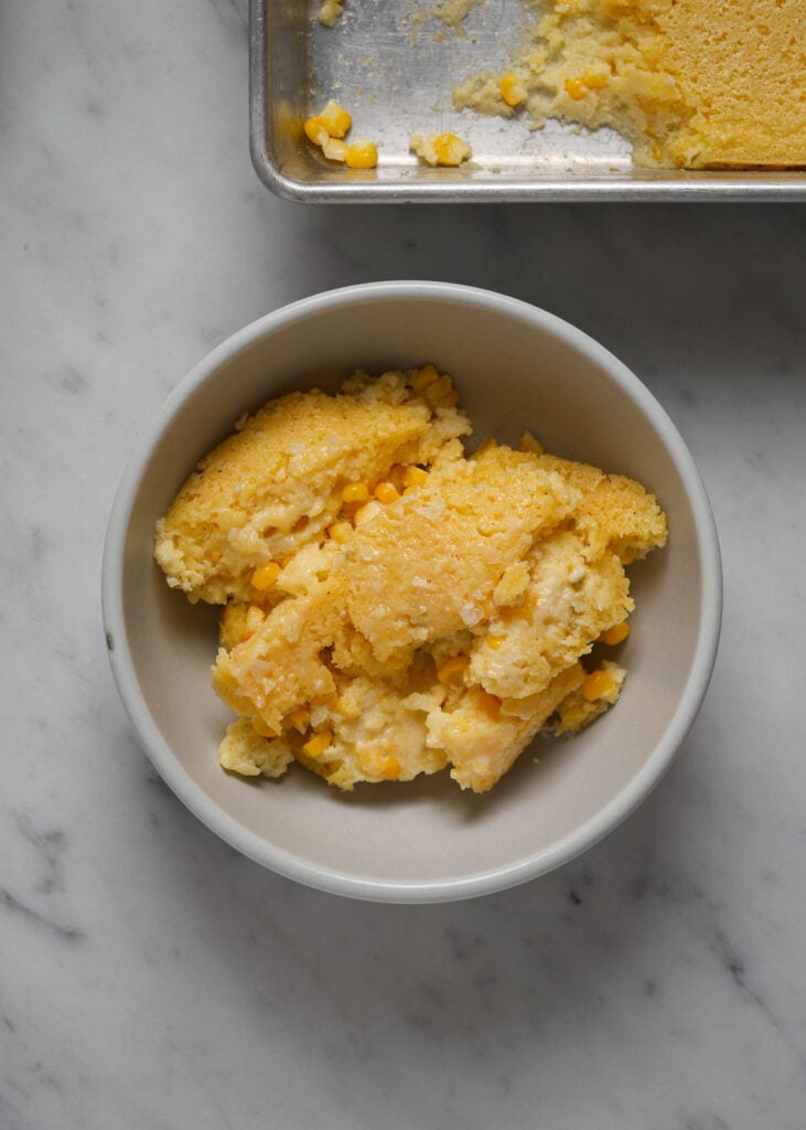 A small bowl of cornbread pudding on a marble tabletop.