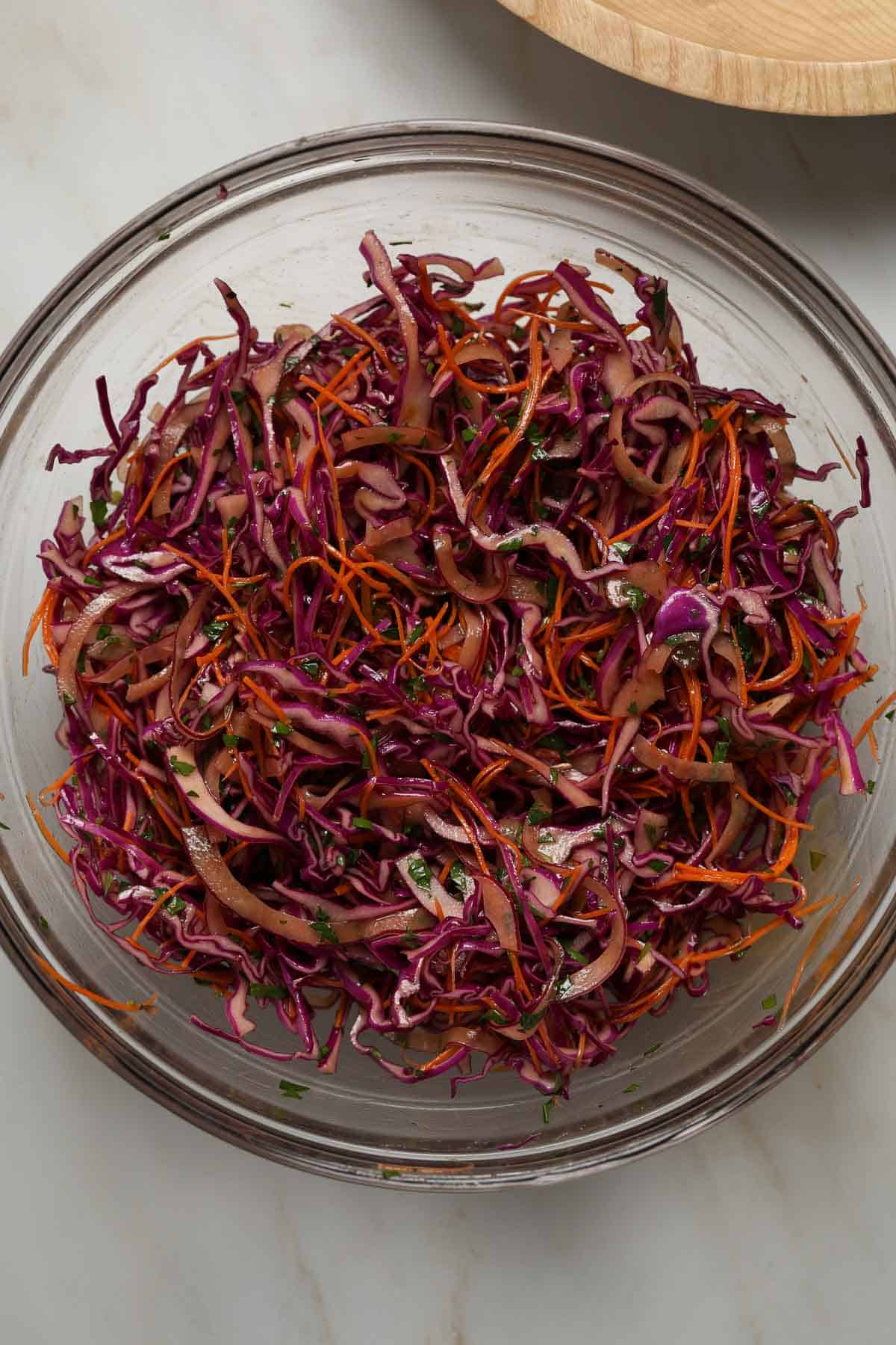 A large, glass, mixing bowl filled with a tossed shredded cabbage salad.