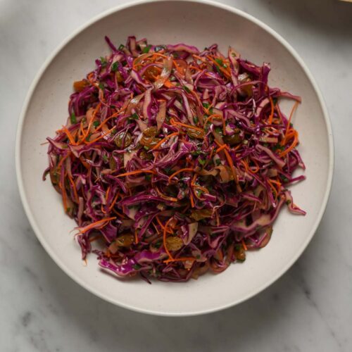 Overhead shot of a purple cabbage salad in a white bowl on a marble table top.