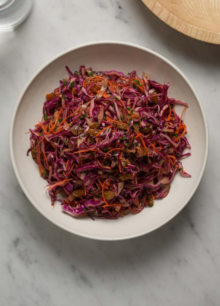 Overhead shot of a purple cabbage salad in a white bowl on a marble table top.