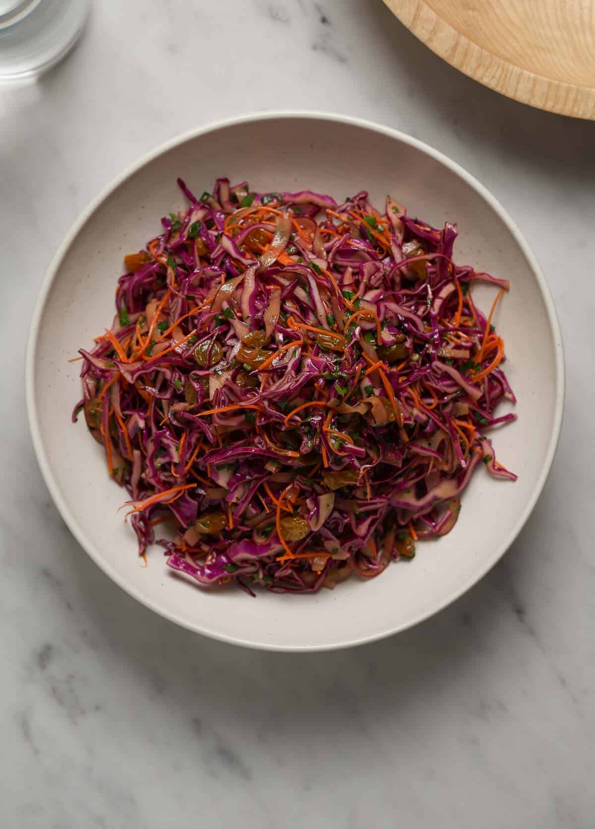 Overhead shot of a purple cabbage salad in a white bowl on a marble table top.