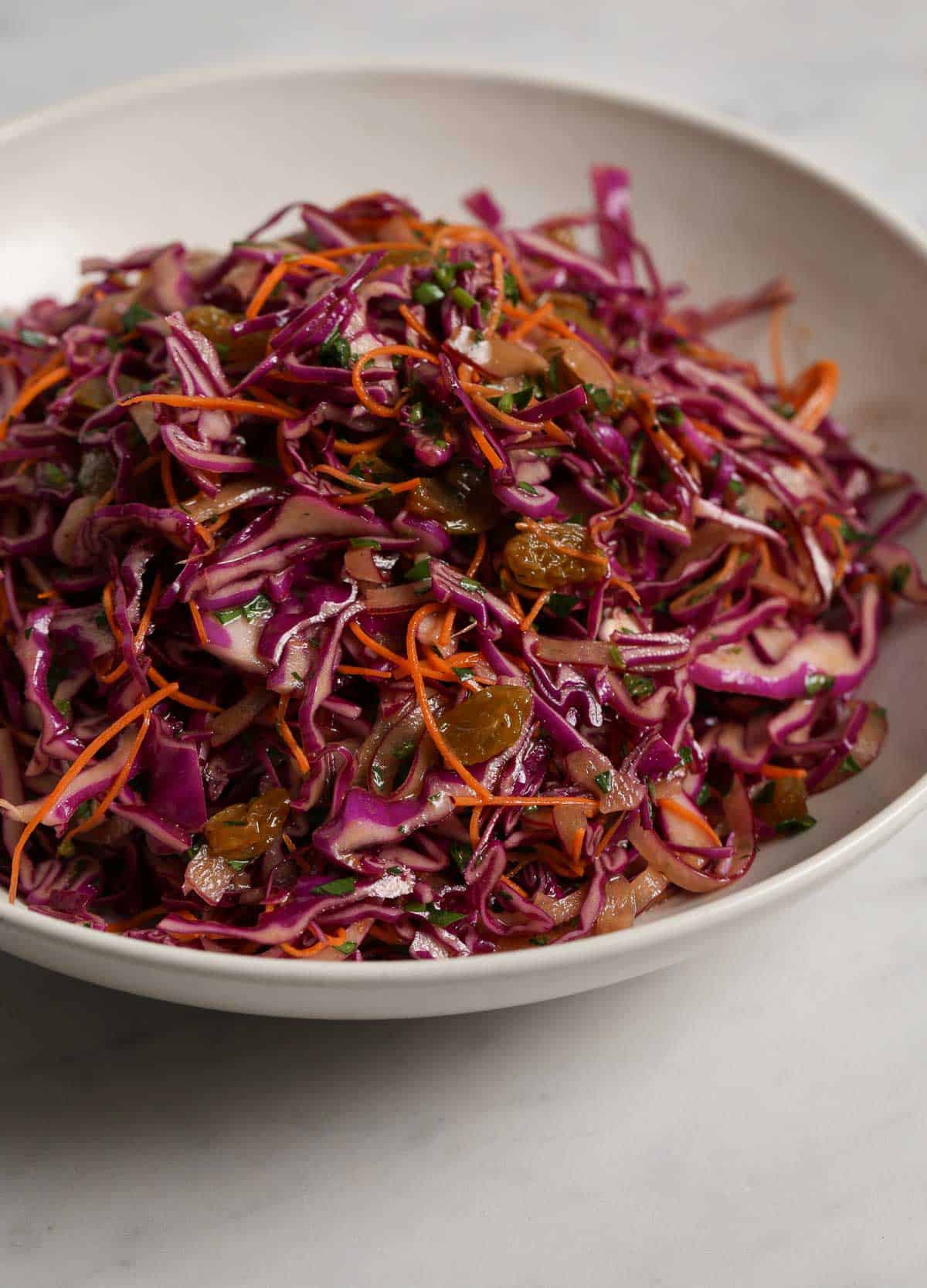 A close up side profile of a vibrant, purple and orange cabbage salad in a white ceramic bowl.