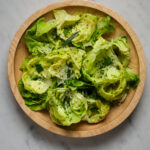 A wooden salad bowl filled with butter lettuce, chives, and fresh herbs.