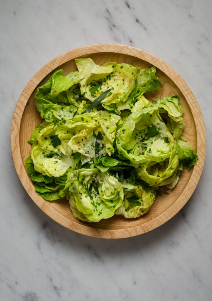 A wooden salad bowl filled with butter lettuce, chives, and fresh herbs.