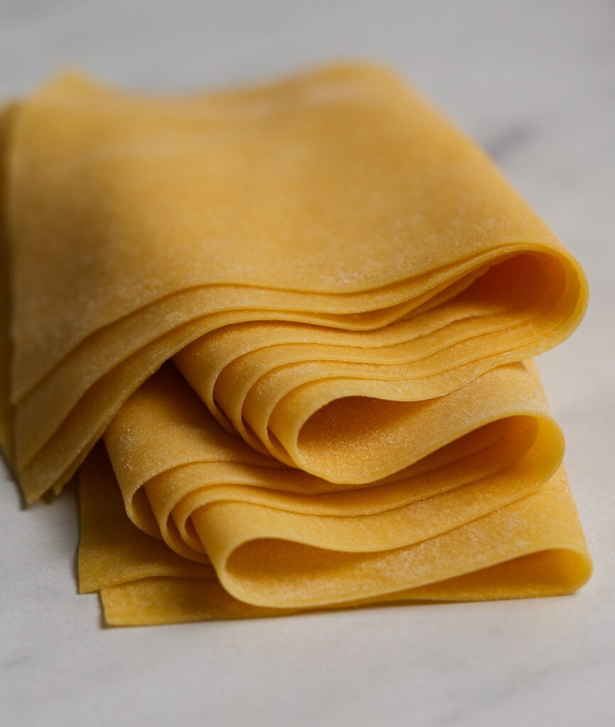 Thin, yellow sheets of fresh pasta dough gently folded on a marble tabletop.