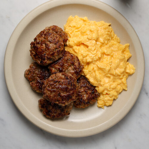 A platter of scrambled eggs and breakfast sausage patties.