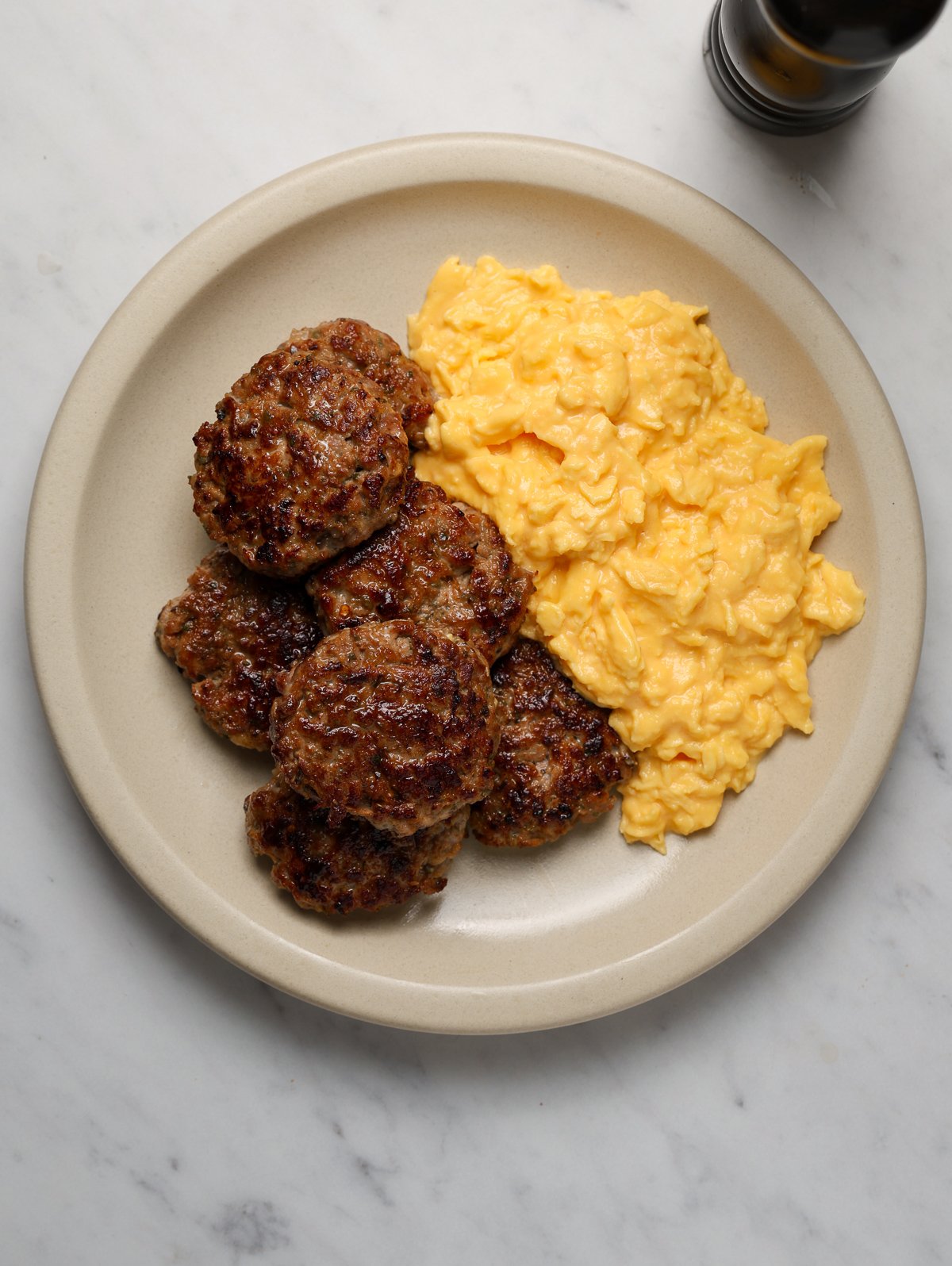 A platter of scrambled eggs and breakfast sausage patties.