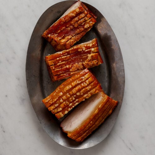 Four portions of pork on an oval, silver platter.