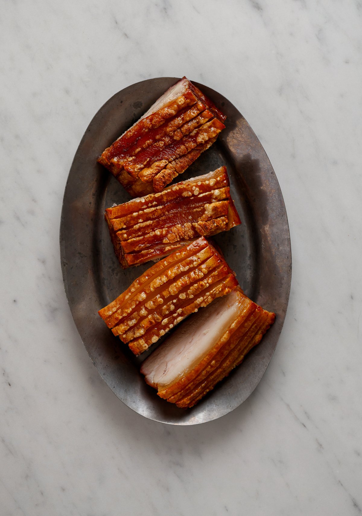 Four portions of pork on an oval, silver platter.