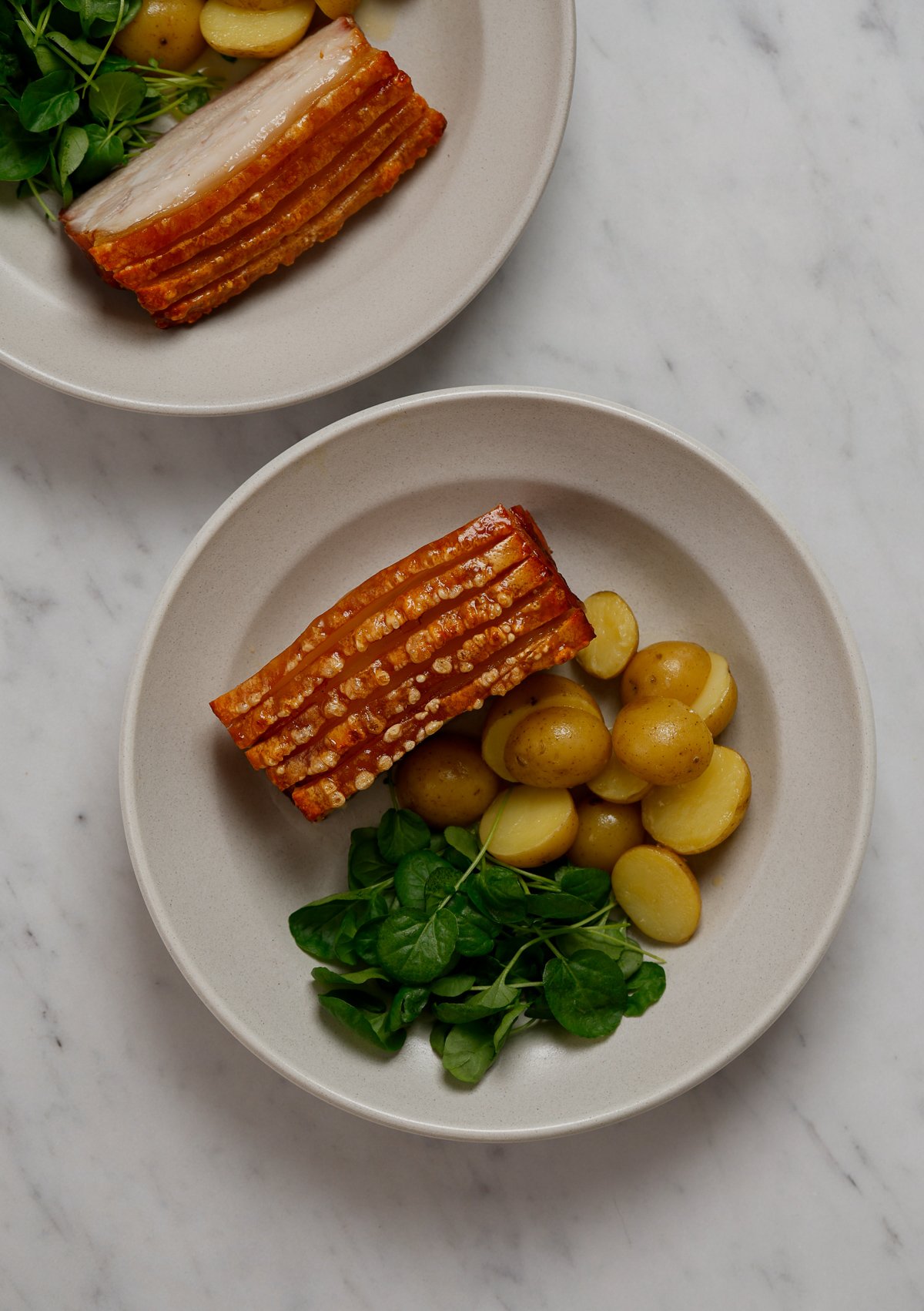 A bowl with a portion of roasted pork, with baby potatoes, and watercress.