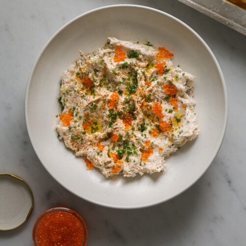 A white bowl of smoked fish dip topped with minced chives and fish roe.