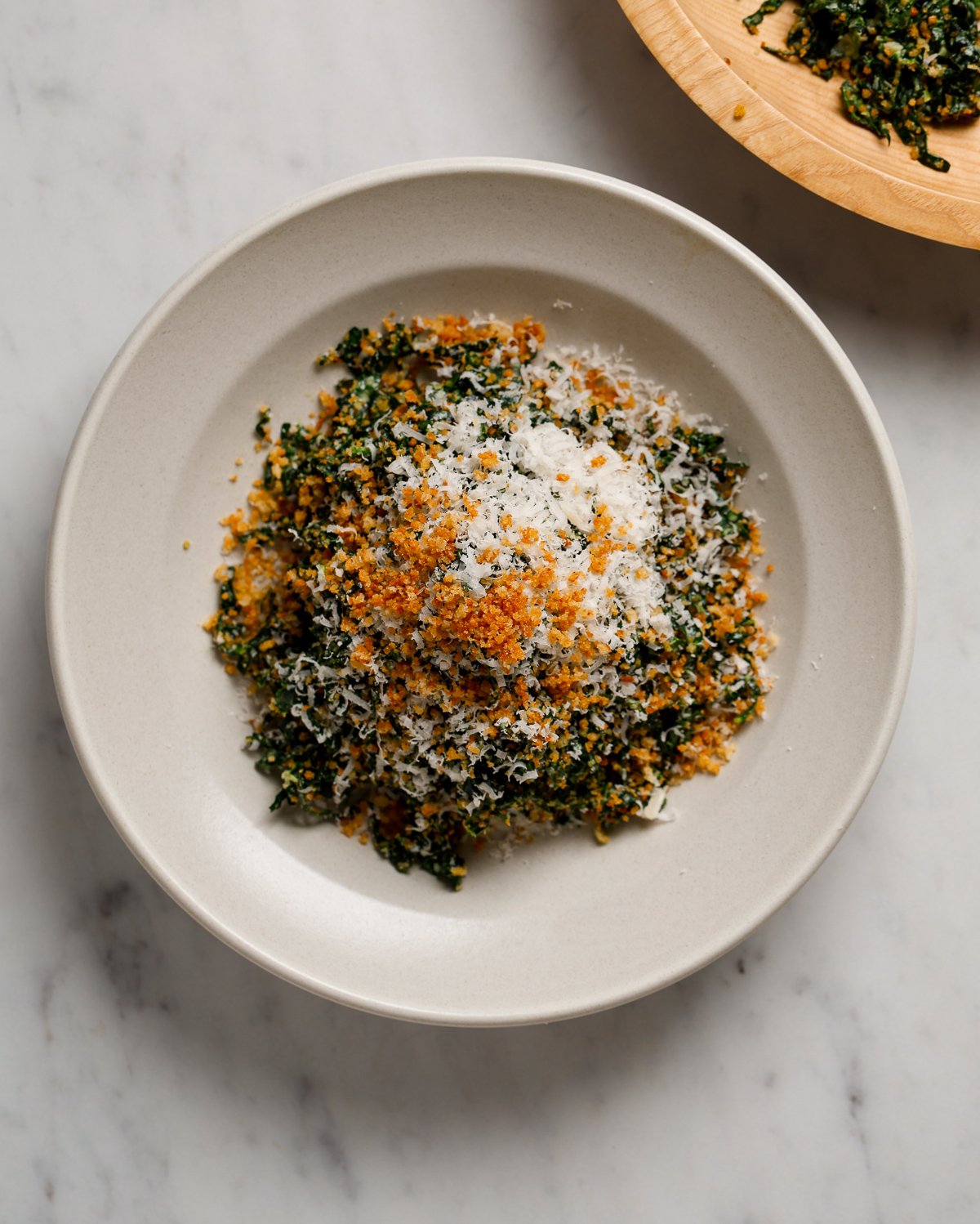 A bowl of Kale Caesar Salad on a white marble table top.