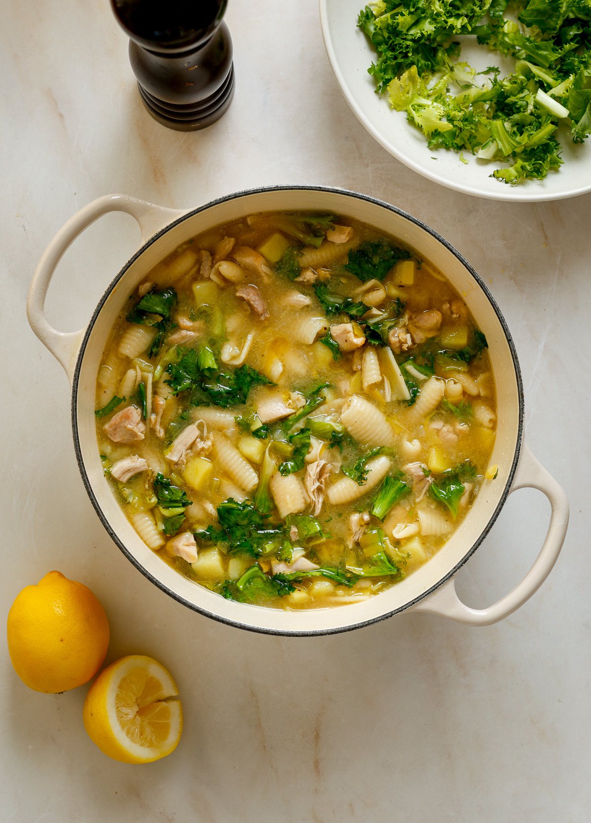 A white cast iron pot filled with soup and surrounded by lemons and a pepper mill.