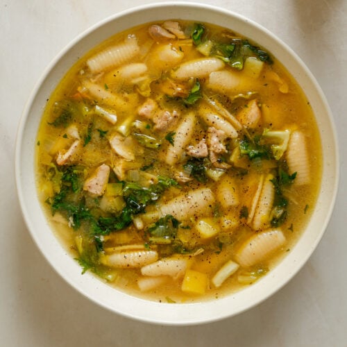 A white bowl filled with soup, pasta, wilted greens and diced potato.