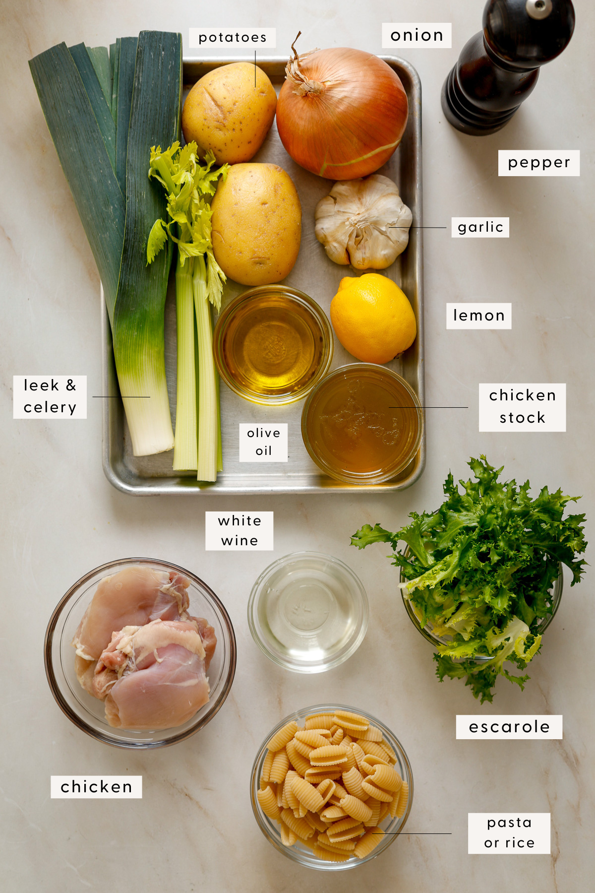 Recipe ingredients on a baking tray: leeks, potatoes, lemon, chicken, escarole etc.